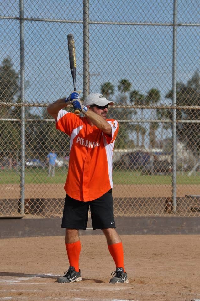 Youth softball player in orange jersey preparing to bat on a dirt field