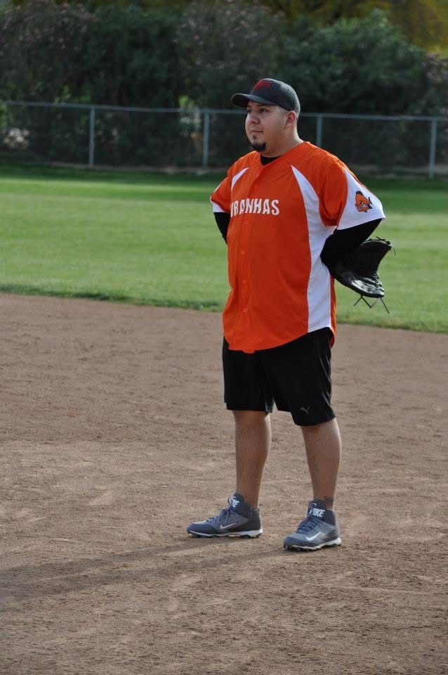 Baseball coach in orange and black uniform standing on a dirt field with a glove under one arm