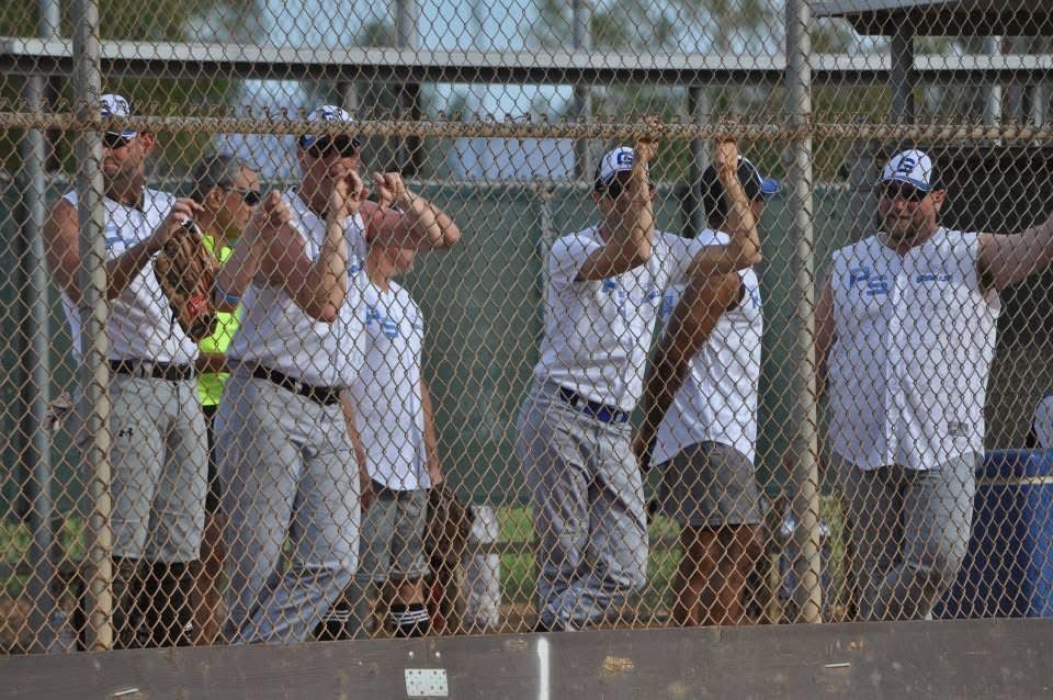 People standing behind a chain-link fence, watching or cheering at an outdoor event.