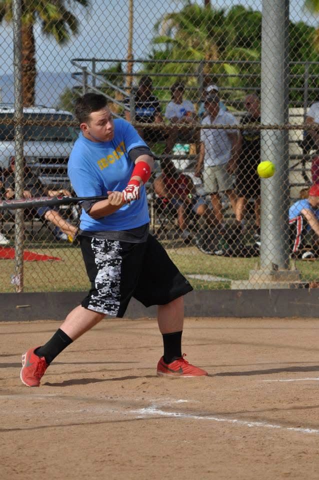Softball player in blue shirt and black shorts swings at a pitch on a dirt field.