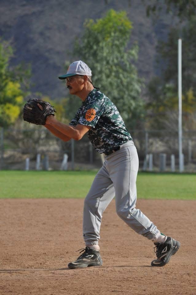 Baseball player in a green camouflage jersey and gray pants preparing to catch a ball on the infield