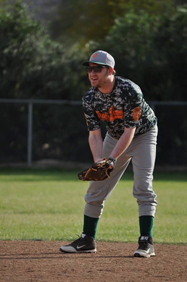 Baseball player in black camouflage jersey and gray pants ready in a fielding stance on a baseball diamond