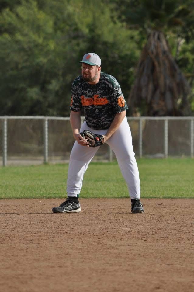 Baseball player in black jersey and white pants crouches ready on the infield dirt.