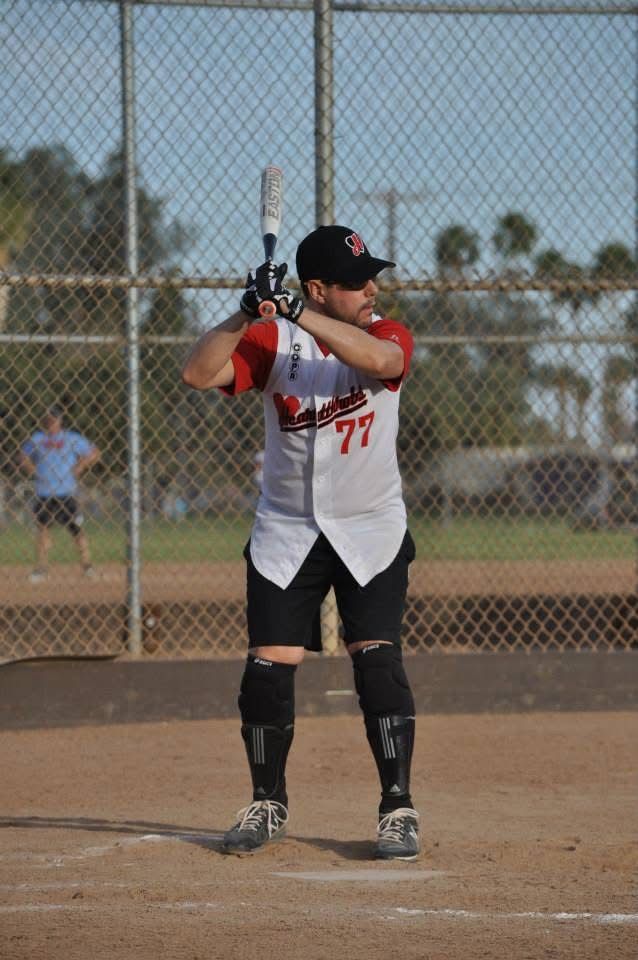 Softball player in white and black uniform at bat on a dirt field
