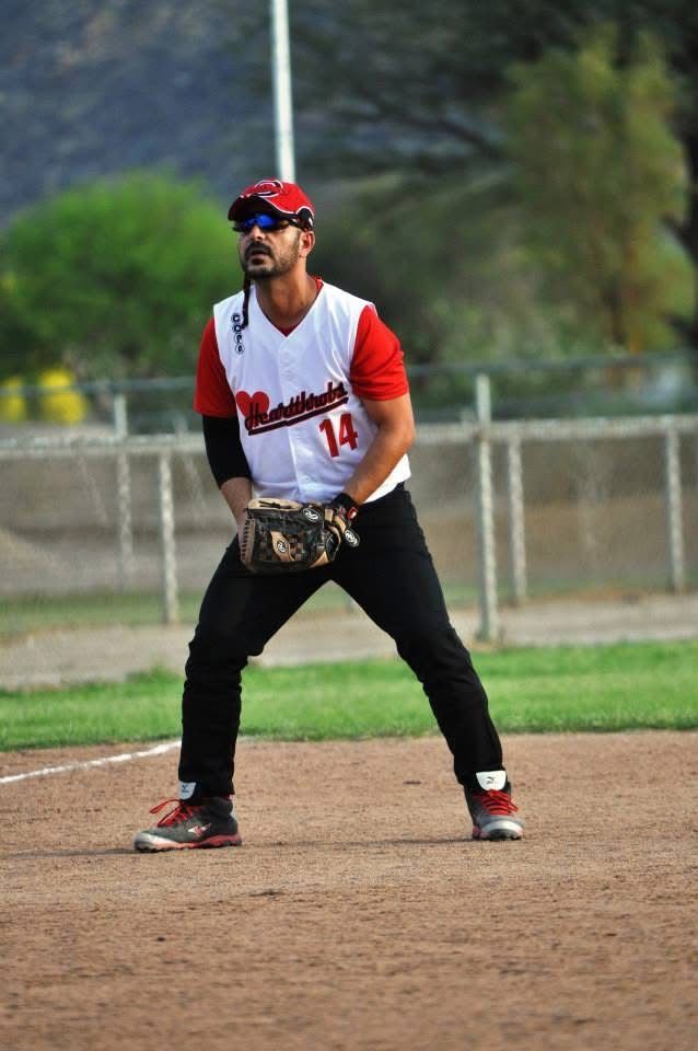 Baseball player in red and white uniform ready in the infield, crouched with glove on a dirt field.
