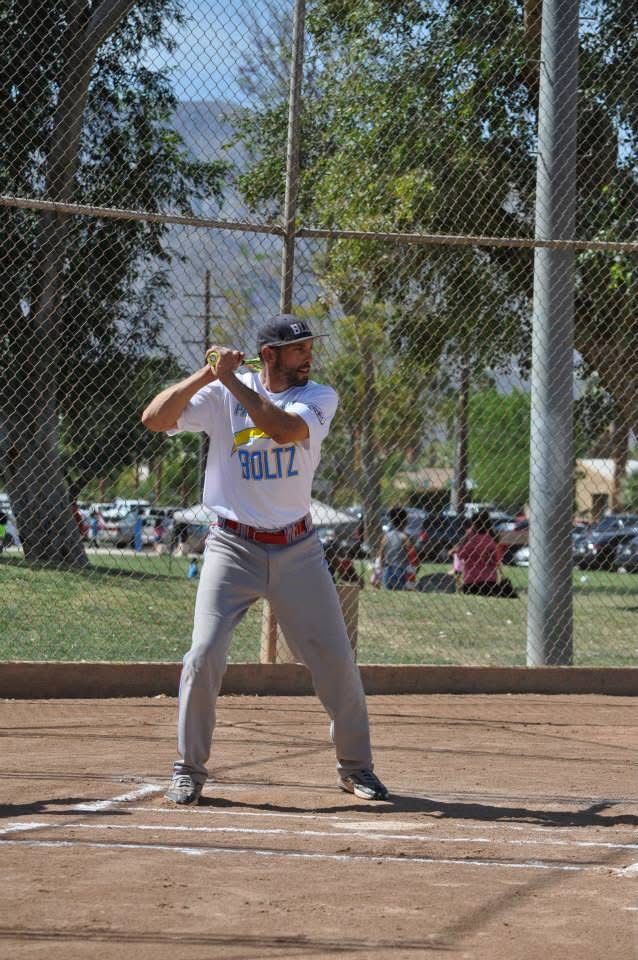 Softball batter in white jersey and gray pants stands in the batter’s box, holding a bat ready to swing.