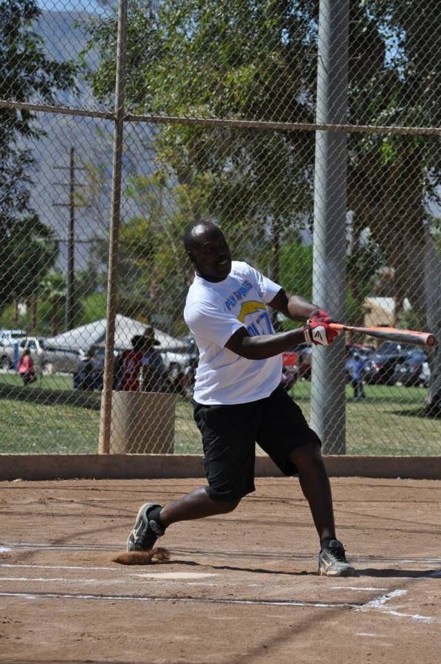 Softball player in white shirt swinging a bat at home plate on a dirt field.