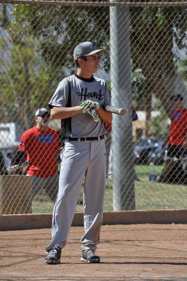 Baseball player in gray uniform holding a bat on a field, standing near a chain-link fence