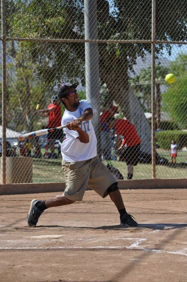 Baseball batter swinging at a pitch on a dirt field near a chain-link fence.