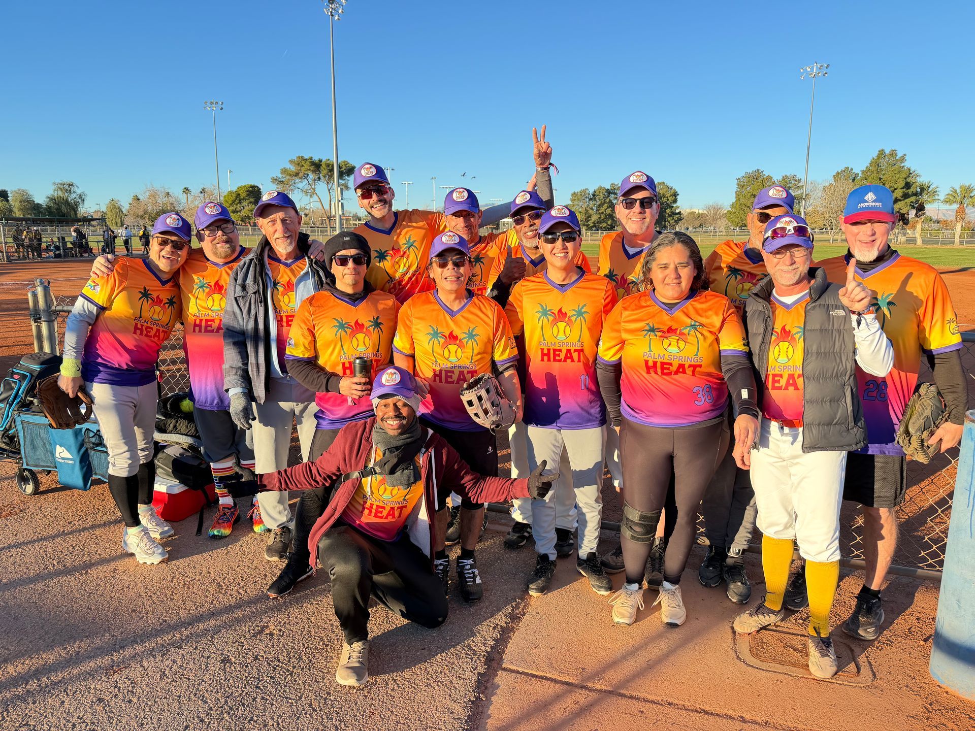 Group of runners in matching orange jerseys posing outdoors at sunrise with a race start in the background