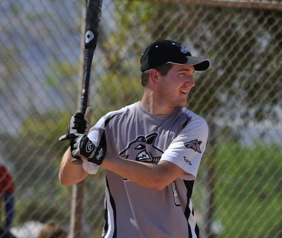 Baseball player in gray jersey and black cap holding a bat at the plate, ready to swing.