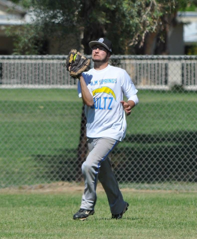 Baseball player in a white jersey and cap catches a ball in the outfield.