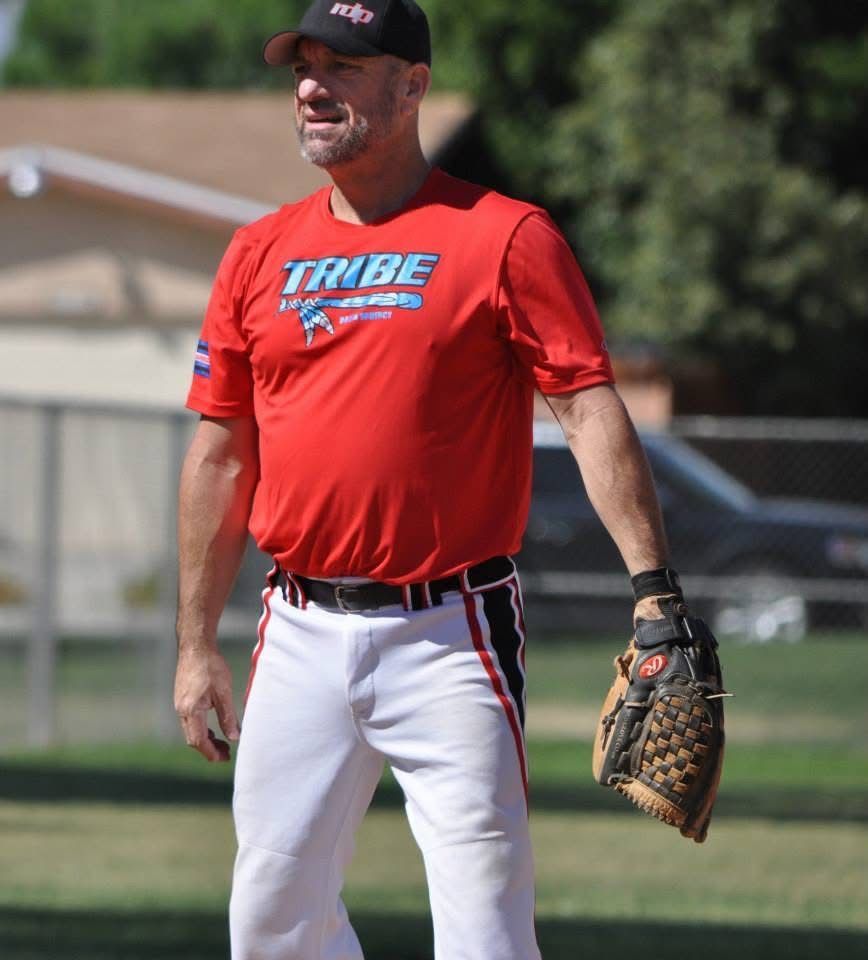 Baseball player in red shirt and white pants standing on a field with a glove on his left hand