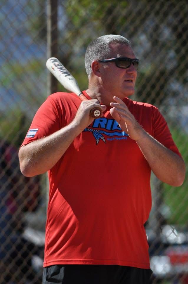 Man in a red shirt holding a baseball bat in a batting stance on a sunny field