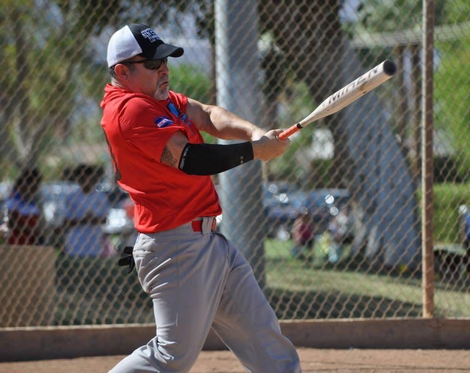 Baseball player in red shirt and gray pants swinging a bat on a field