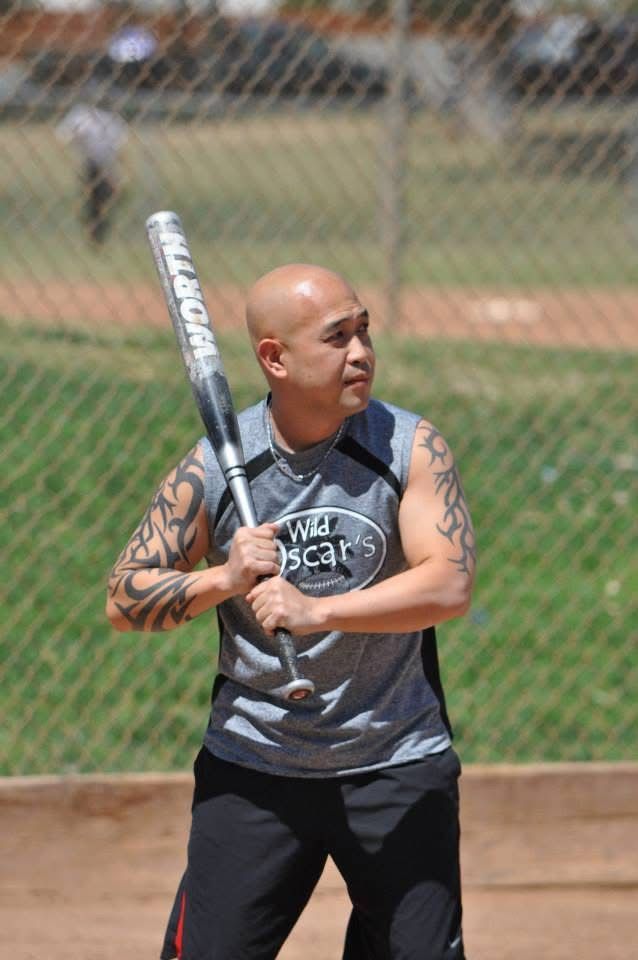 Man holding a baseball bat at a field, preparing to swing, with a chain-link fence in the background