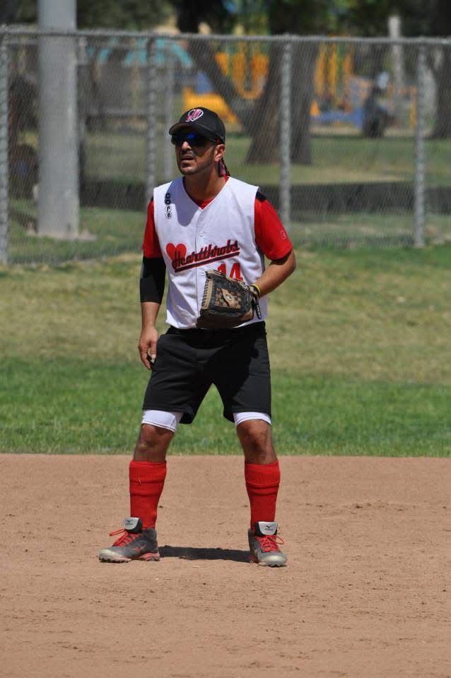 Baseball infielder in red and white uniform standing on a dirt field, ready to field a ball