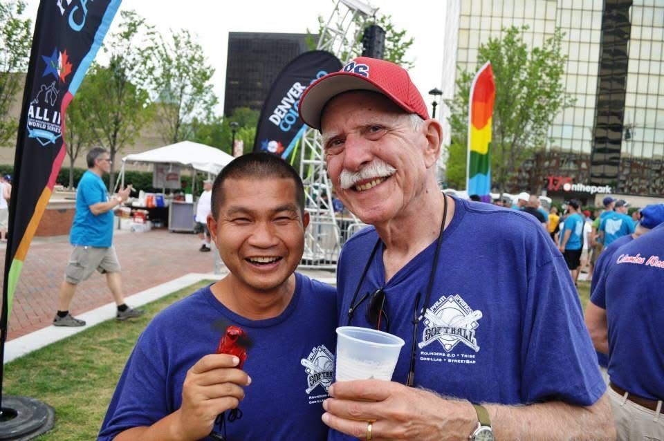 Two smiling runners in blue shirts pose outdoors at a race event, holding drinks.