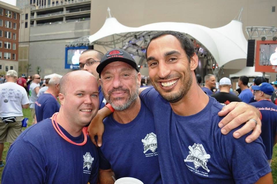 Three men in blue shirts smiling and posing together at an outdoor event
