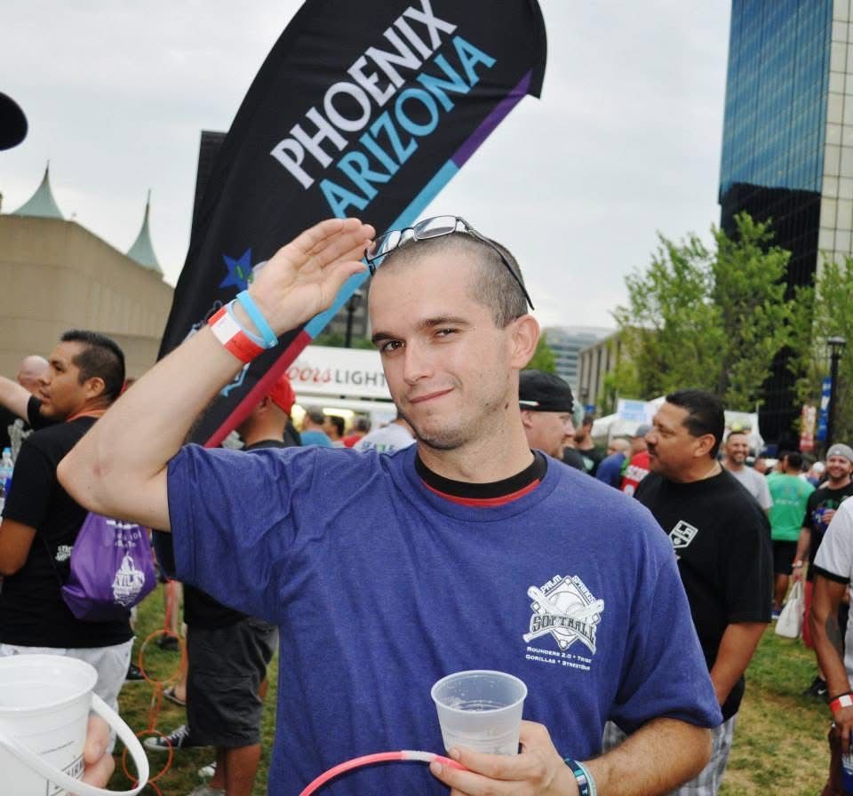 Man in a blue shirt holding a cup and a Phoenix Arizona sign at an outdoor event