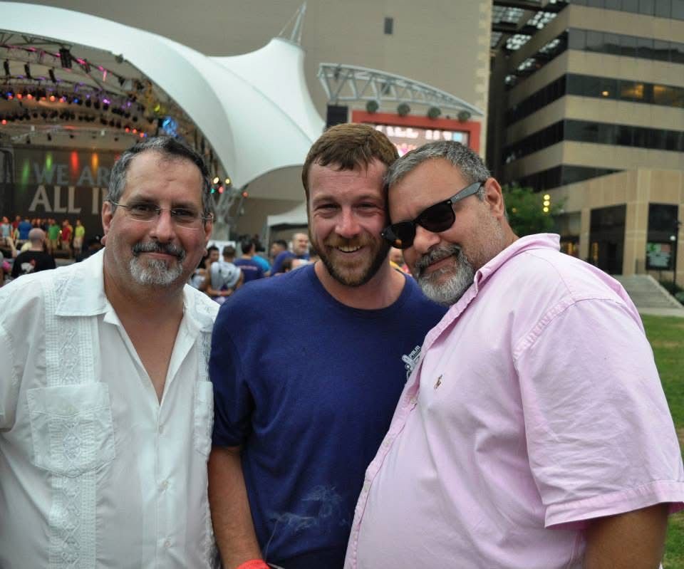 Three smiling people posing outdoors in front of a stadium or event venue