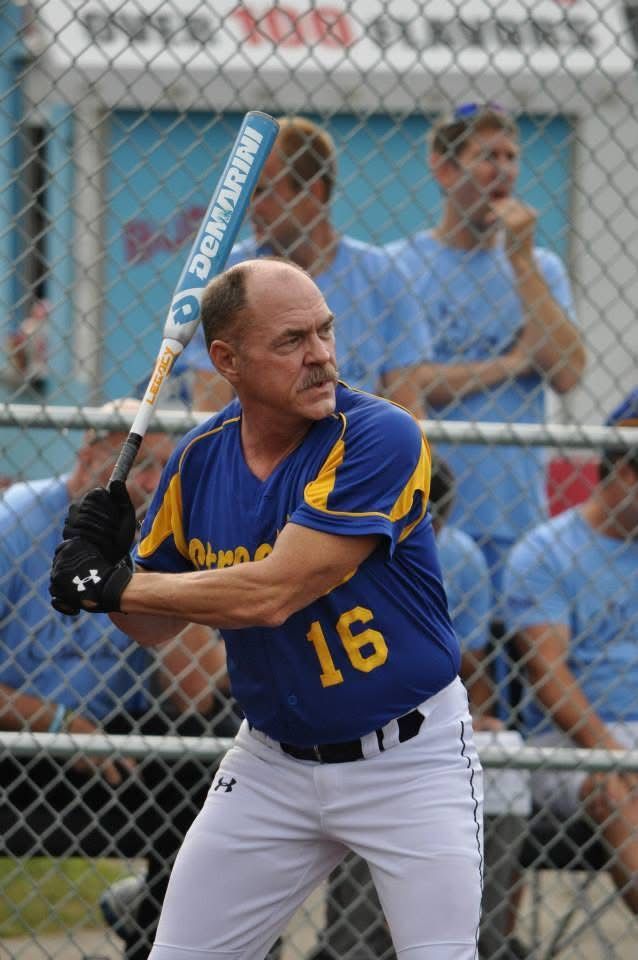 Baseball player in blue-and-yellow uniform at bat, holding a bat in front of a chain-link fence.