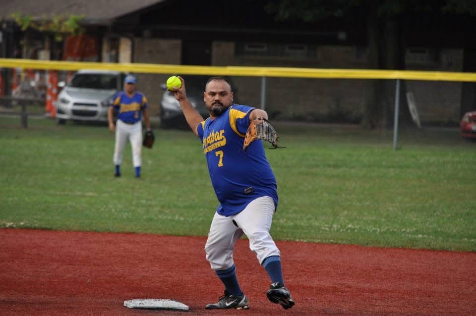 Softball pitcher in blue and white uniform throws from the mound on a grassy field.