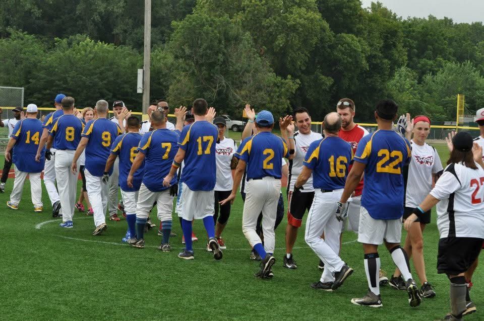 Baseball players in blue and white uniforms walk across a grassy field after a game.