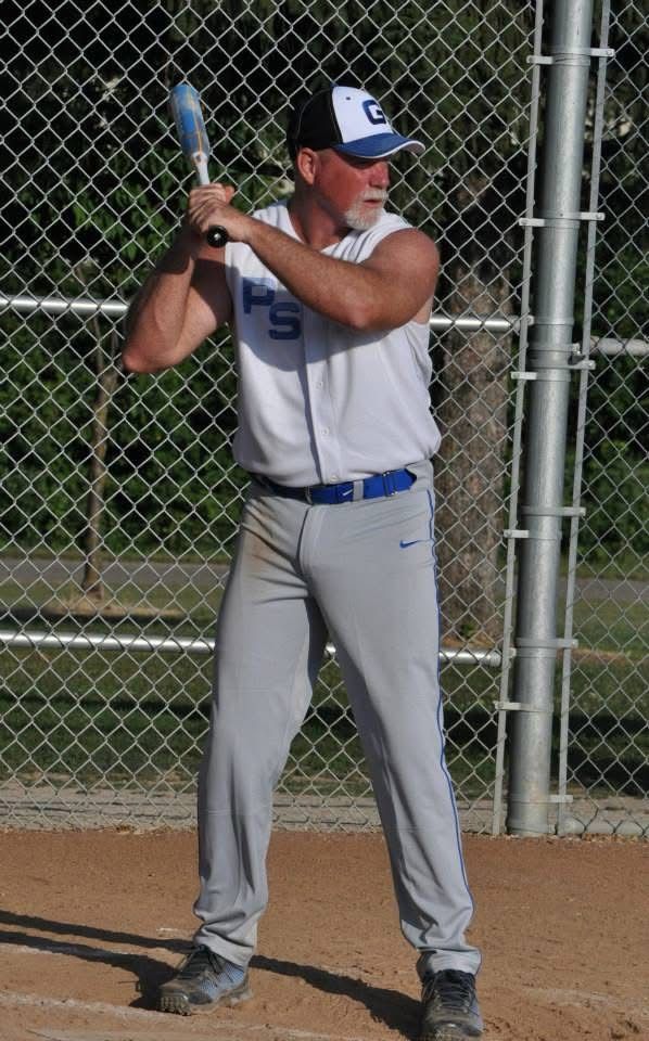 Baseball player in gray uniform holding a bat in a batting stance on a field, with a chain-link fence behind.