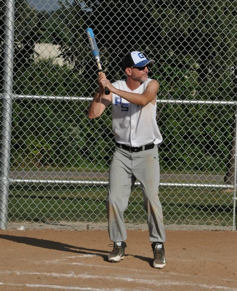 Baseball player at bat in gray uniform, holding a bat in front of a chain-link fence.
