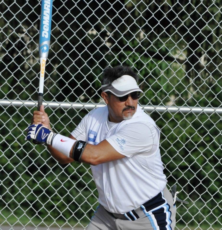 Softball player in white uniform and visor holding a bat at the fence, ready to swing
