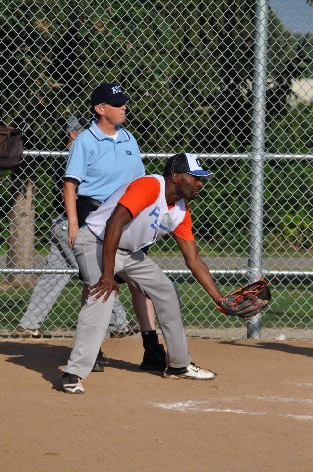 Baseball player in gray and orange bends to field a ground ball, with an umpire behind him.
