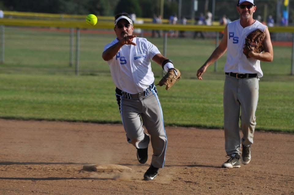 Two baseball players in gray uniforms field a bright yellow ball on a dirt infield.