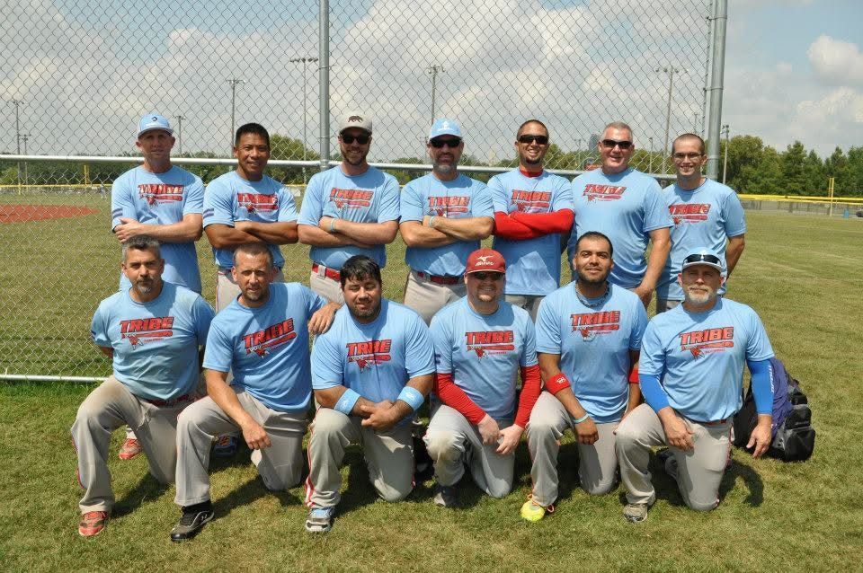 Men’s baseball team posing on a grassy field, wearing light blue jerseys and gray pants.