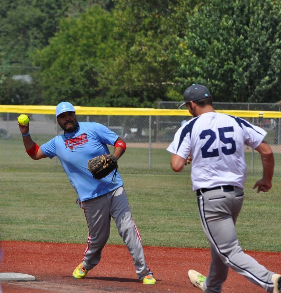 Two softball players on a field, one catching a ball while the other runs toward first base.