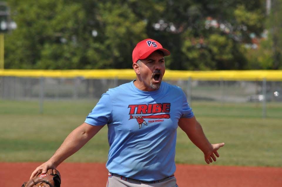 Man in blue shirt and red cap celebrating on a softball field with glove in hand