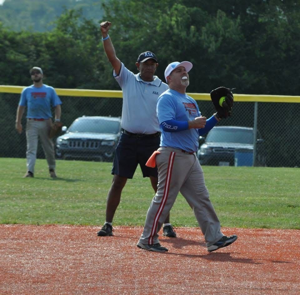 Umpire signaling out as a softball player in blue walks on the field near home plate