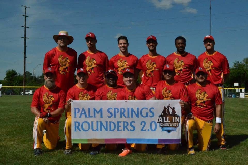 Baseball team in red uniforms posing with a “Palm Springs Rounders 2.0” banner on a field