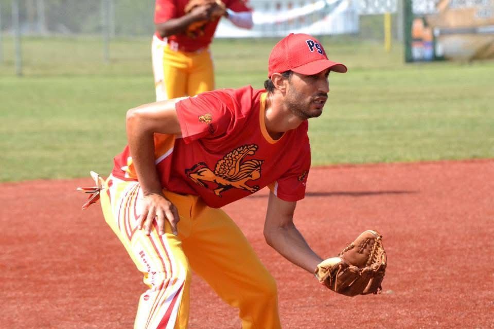 Baseball player in red and yellow uniform crouches on a dirt field, ready to field a ball