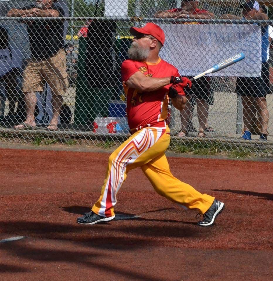 Baseball player in red and yellow uniform swinging at a pitch on a dirt field
