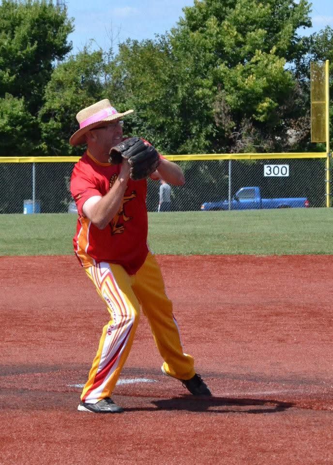 Baseball pitcher in red and yellow uniform on the mound, mid-throw on a sunny field