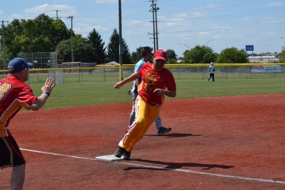 Baseball player in red and yellow sprints past home plate as catcher reaches for the ball on a sunny field