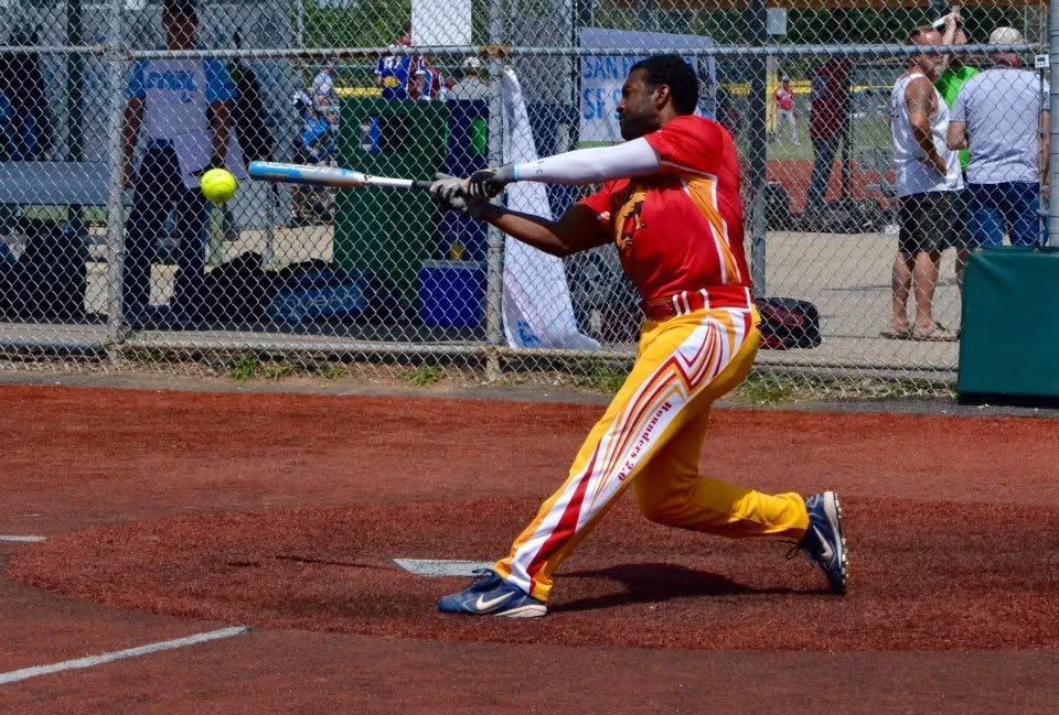 Baseball player in red and yellow uniform swinging at a pitch on a dirt field