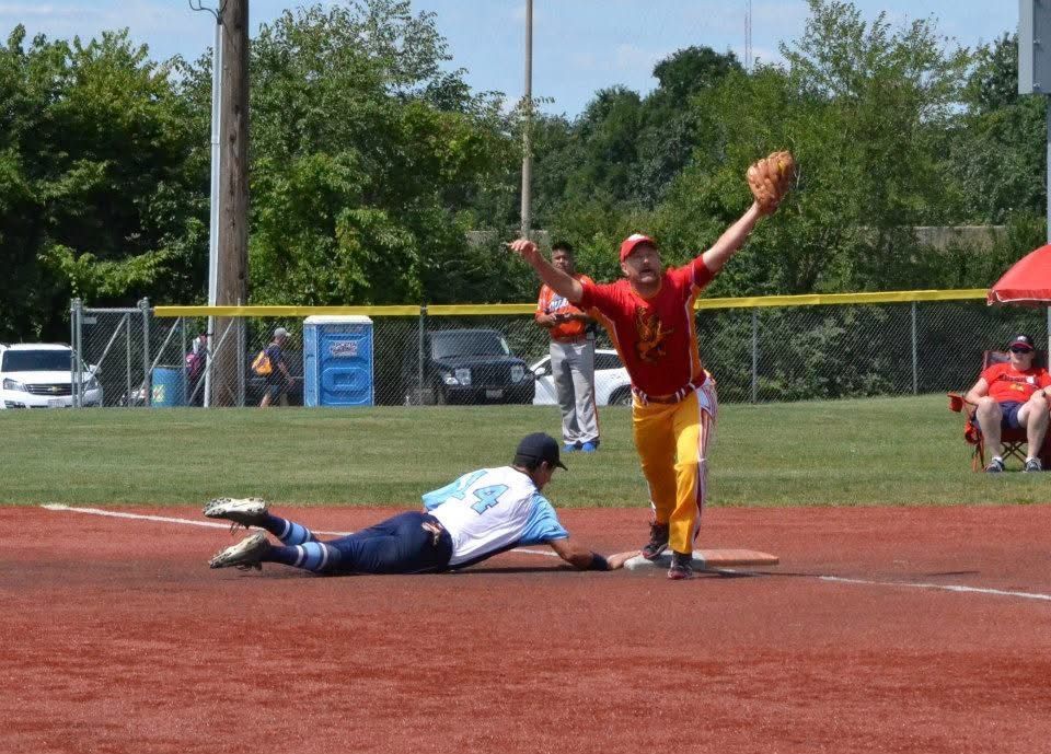 Baseball player in red tags a runner sliding into home plate on a sunny field
