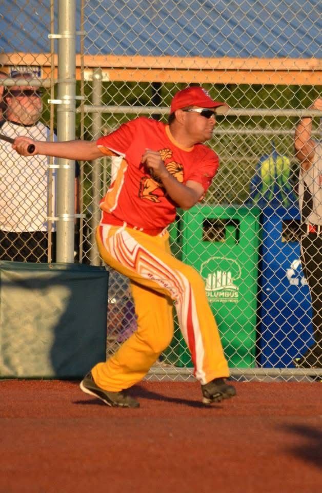 Baseball player in red uniform swinging near a chain-link fence at a field