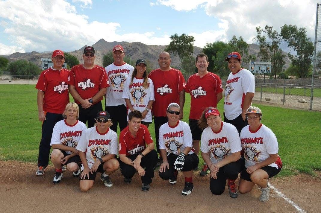 Baseball team posing on a dirt field, wearing red and white jerseys with mountains and sky in the background