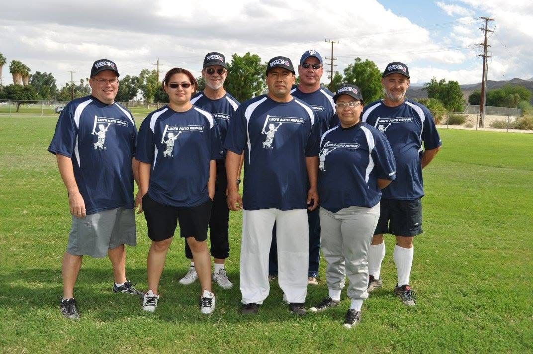 Seven people in matching navy shirts and caps stand together on a grassy field.