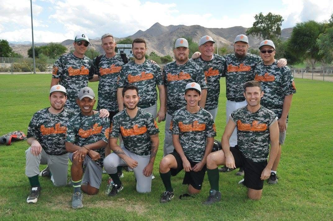 Baseball team in matching camouflage jerseys posing on a grassy field with mountains in the background