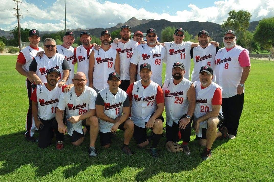 Group of baseball players in white and red uniforms posing on a grassy field with mountains in the background