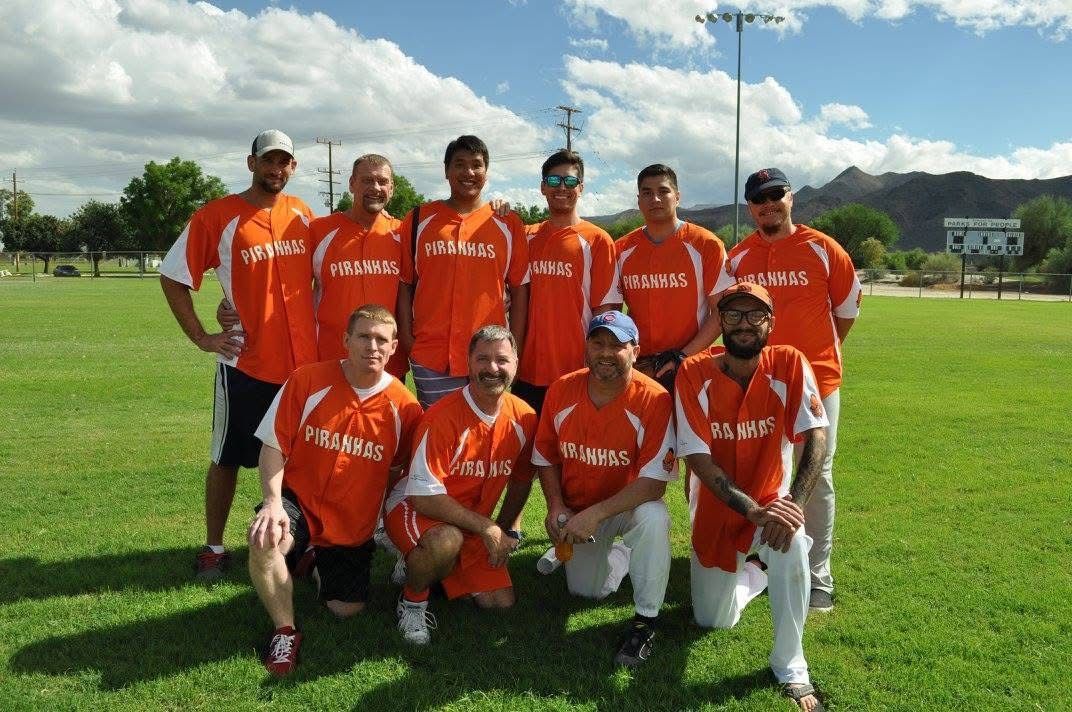 Cricket team in orange uniforms posing on a grassy field under a bright sky